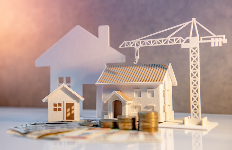 Real estate or property development. Construction business investment concept. Home mortgage loan rate. Coin stack on international banknotes with house and construction crane models on the table.
